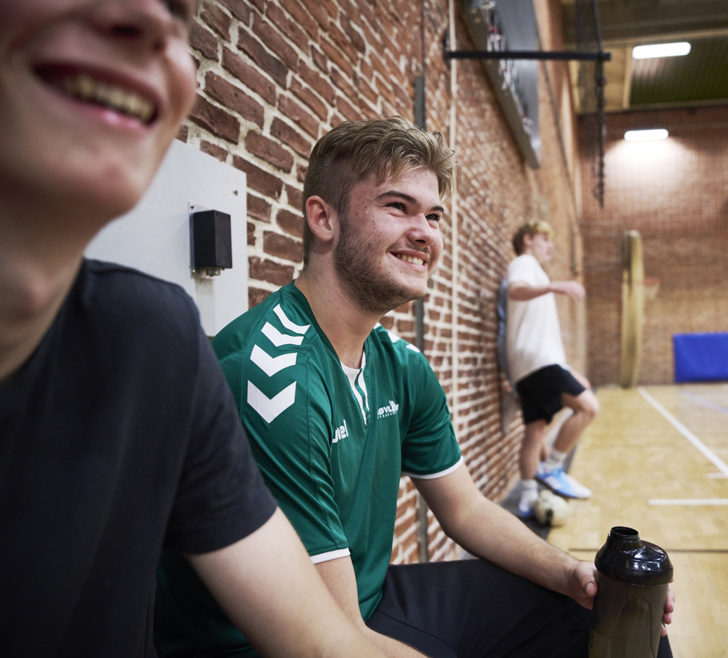 Smilende elever sidder på sidelinjen til idræt