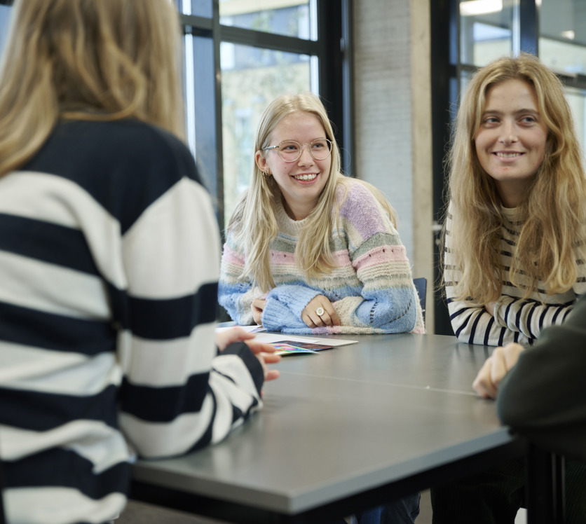 Smilende elever snakker omkring et bord