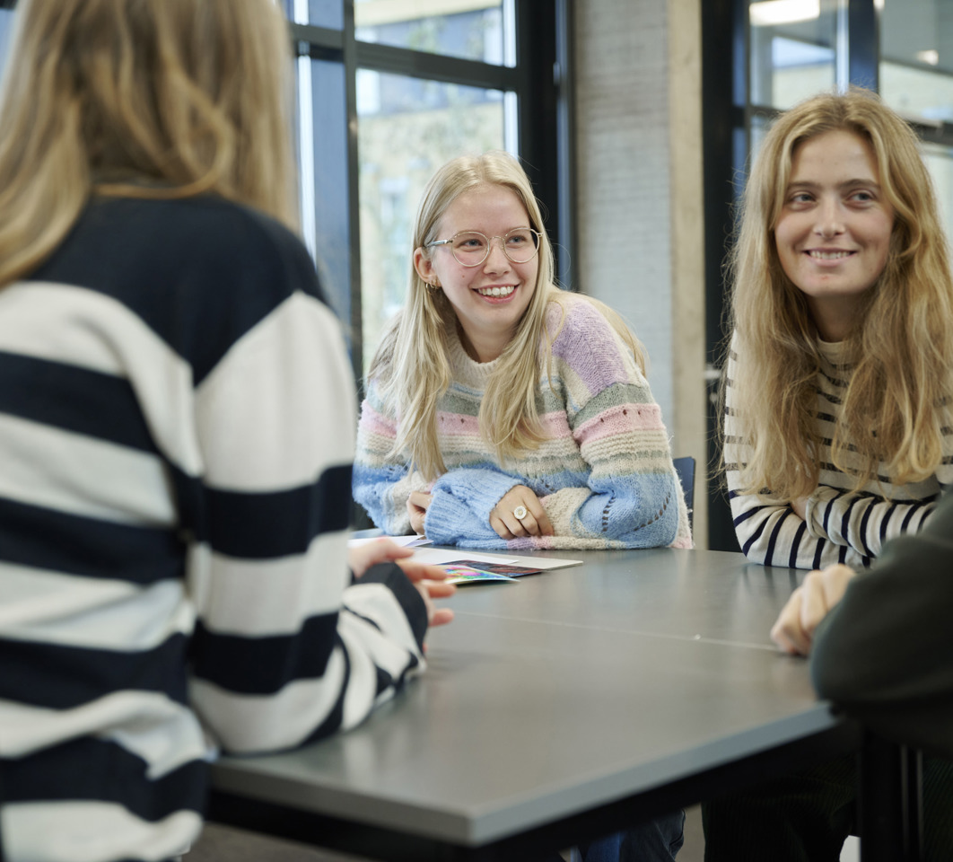 Smilende elever snakker omkring et bord