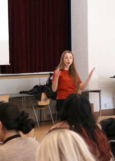 Person taler foran en masse personer i fællessal 