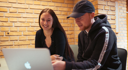 To elever smiler ved et bord med computer 