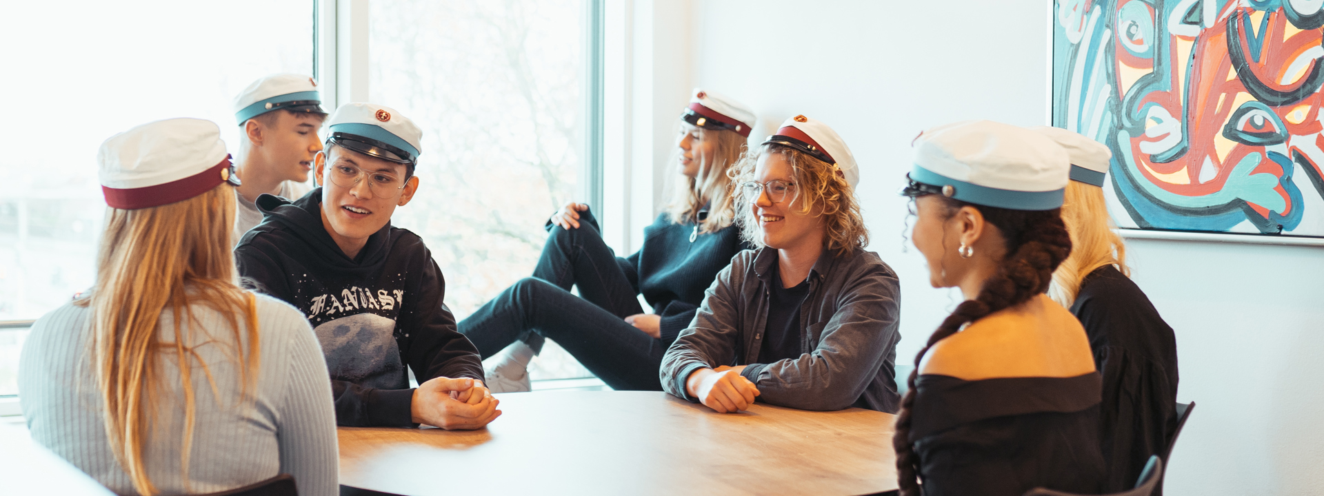 Glade elever med studenterhuer sidder omkring gruppebord
