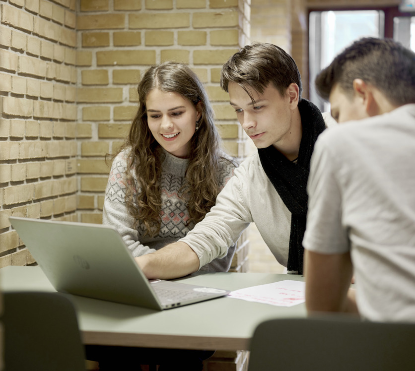Tre glade elever sidder omkring en computer