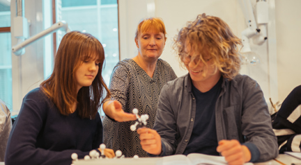 To glade elever får hjælp af underviseren til biologi