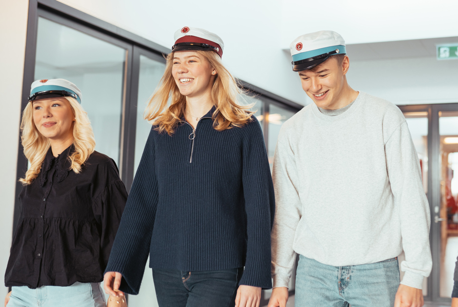 Tre glade elever går sammen med deres studenterhuer på