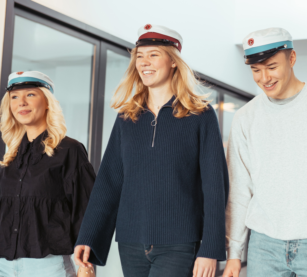 Tre glade elever går sammen med deres studenterhuer på
